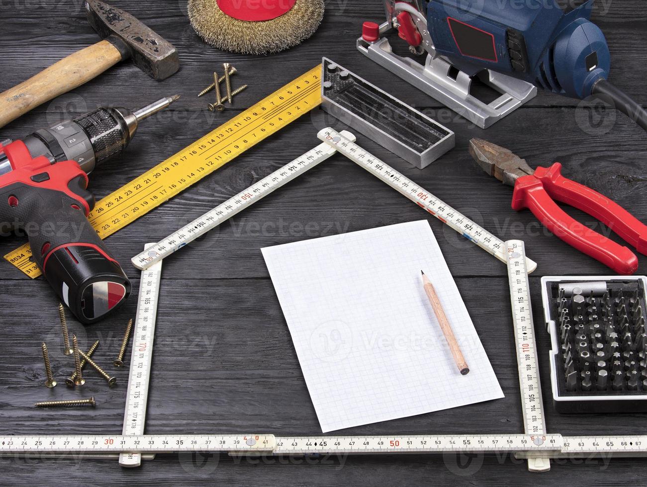 verktyg för konstruktion och reparation på en svart träbakgrund runt ett vitt pappersark med en penna foto
