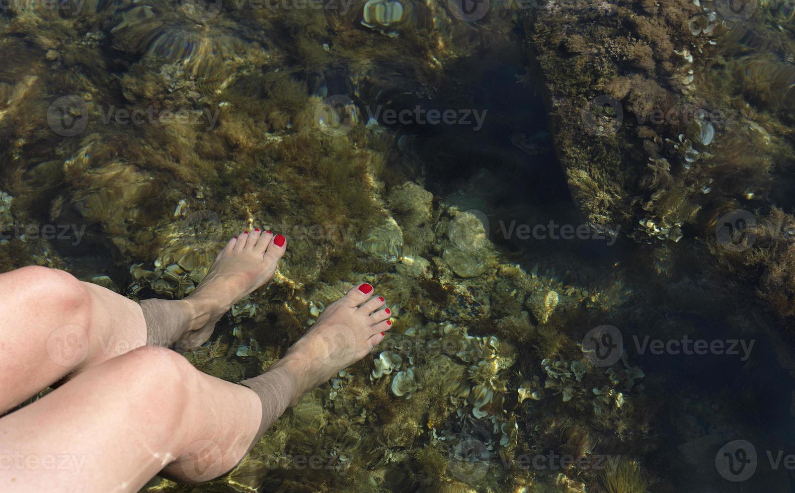 kvinnliga ben med en röd pedikyr sänks ner i det marina genomskinliga vattnet i Adriatiska havet foto