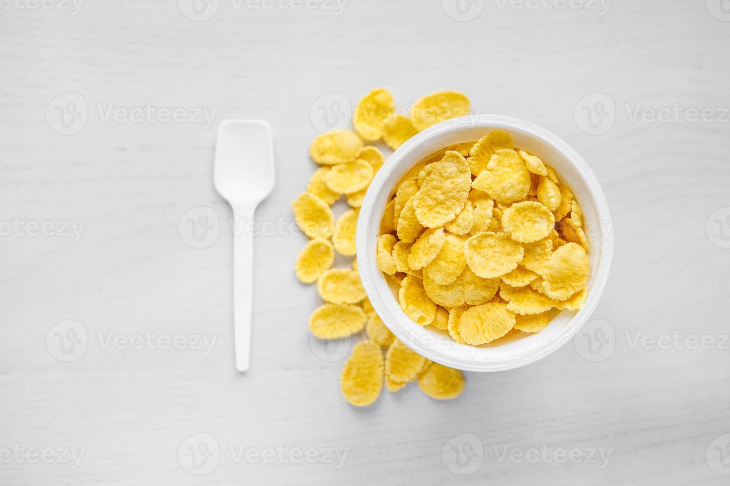 cornflakes i vit skål med sked på vit trä bakgrund foto