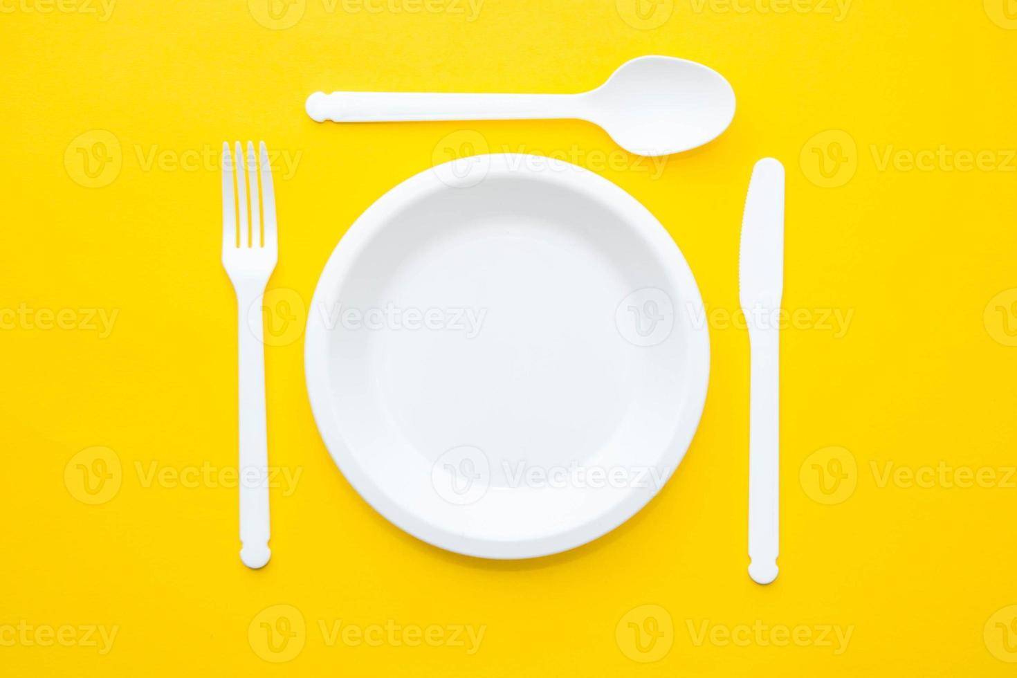 plast vit gaffel, kniv, sked och tallrik på gul bakgrund foto