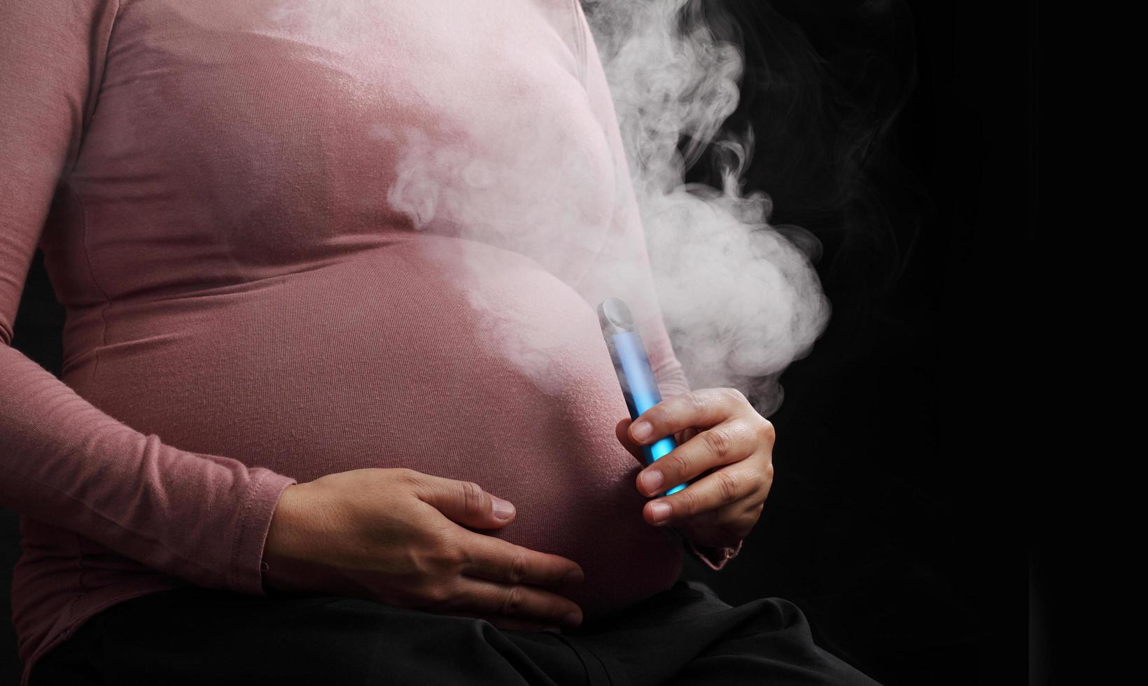 närbild gravid kvinna röker e-cigarett på svart bakgrund foto