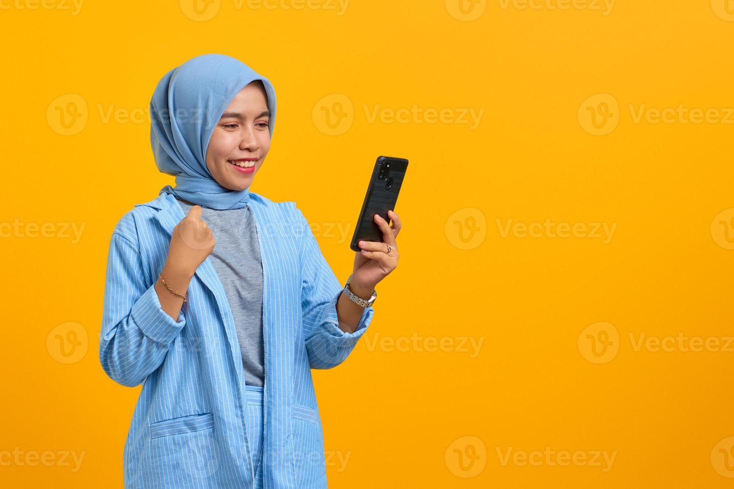 glad ung asiatisk kvinna tittar på mobiltelefon isolerad över gul bakgrund foto