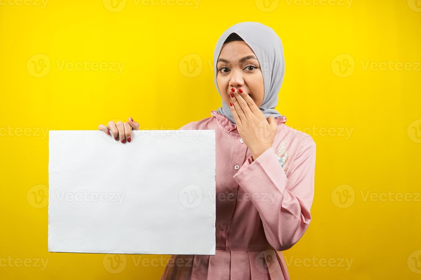 ganska ung muslimsk kvinna förvånad, hand som håller en tom banderoll, plakat, vit tavla, tom skylttavla, vit reklamtavla, presenterar något i kopieringsutrymmet, marknadsföring foto