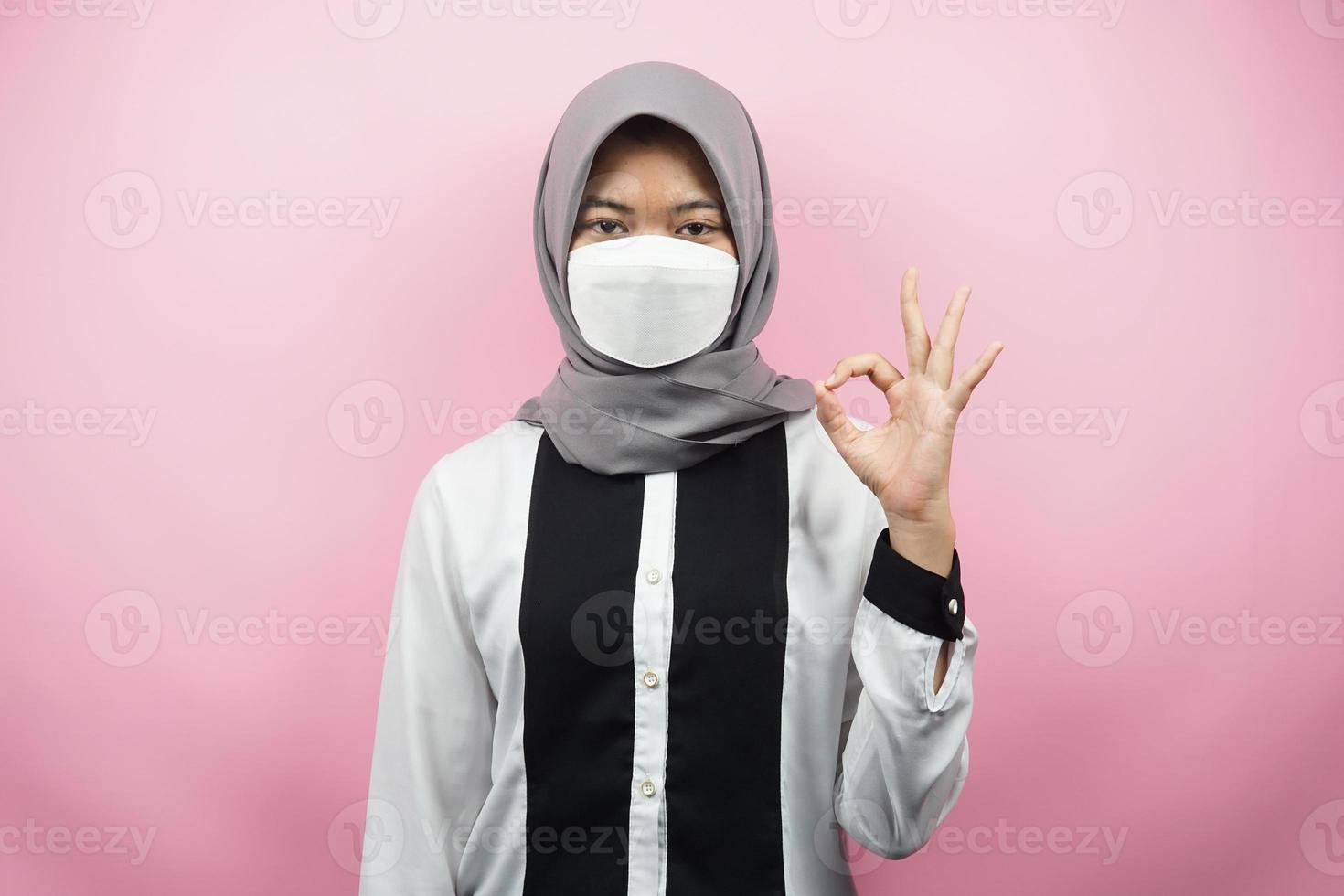 muslimsk kvinna som bär vita masker, anti-coronavirusrörelse, anti covid-19-rörelse, hälsorörelse som använder masker, med händer som visar ok-tecken, bra arbete, framgång, seger, isolerad på rosa bakgrund foto