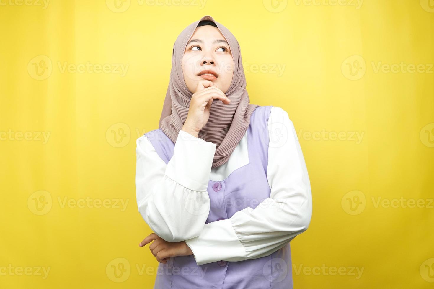 vacker asiatisk ung muslimsk kvinna som tänker, letar efter idéer, letar efter lösningar på problem, med händer som håller kinderna, isolerad på gul bakgrund foto