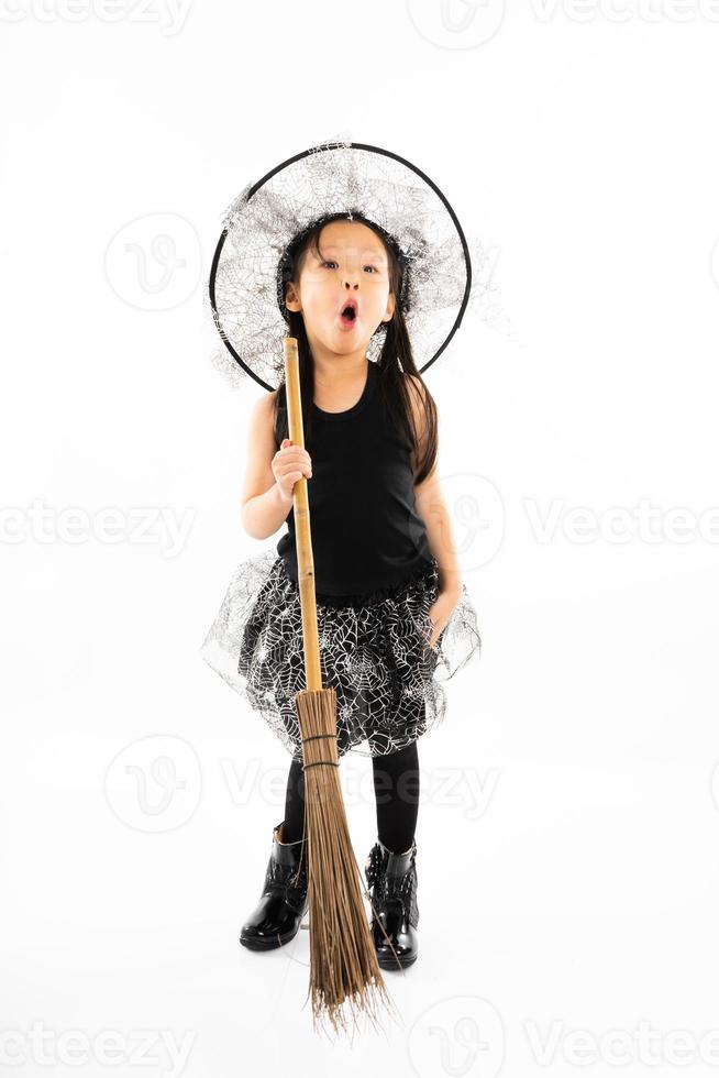 porträtt asiatisk liten flicka klädd i söt häxa för halloween kostym med kvast och isolerad bakgrund foto