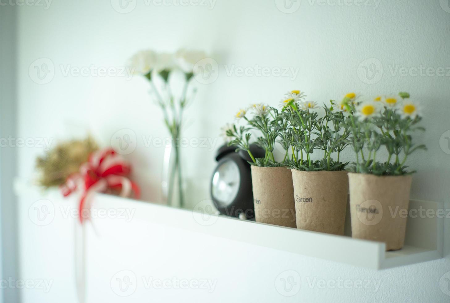 vintage väckarklocka sätter på den vita trähyllan dekorerad av blommorna i keramik foto