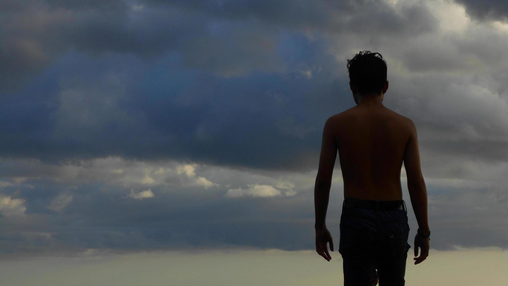 bakifrån av en man utan bar överkropp mot en dimmig himmel bakgrund foto