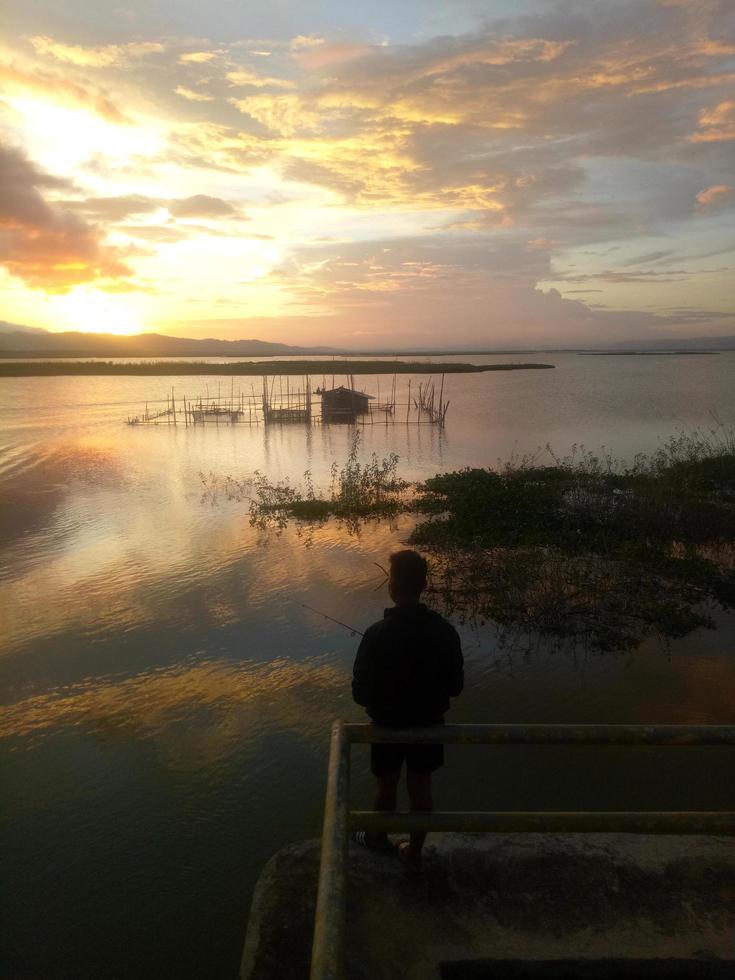 man fiskare som fiskar med ett spinnspö i sjön på eftermiddagen. solnedgång på limboto sjön, Indonesien foto