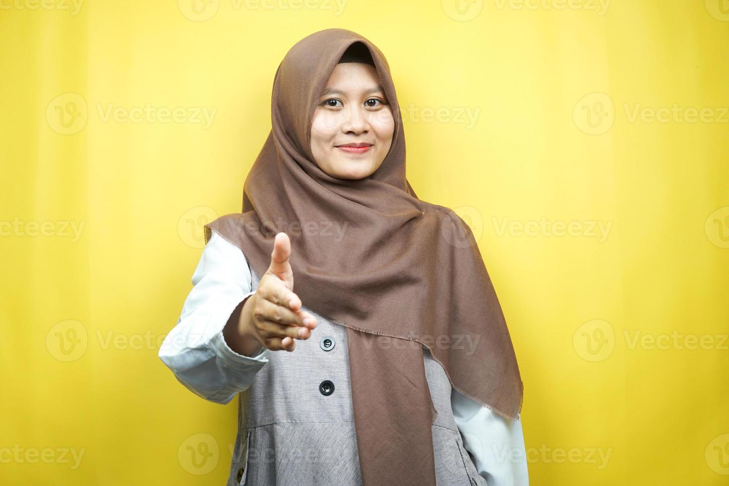 vacker ung asiatisk muslimsk kvinna som ler självsäkert, med händer som skakar kameran, händer tecken på samarbete, hand tecken på avtal, hand tecken på vänskap, isolerad på gul bakgrund foto