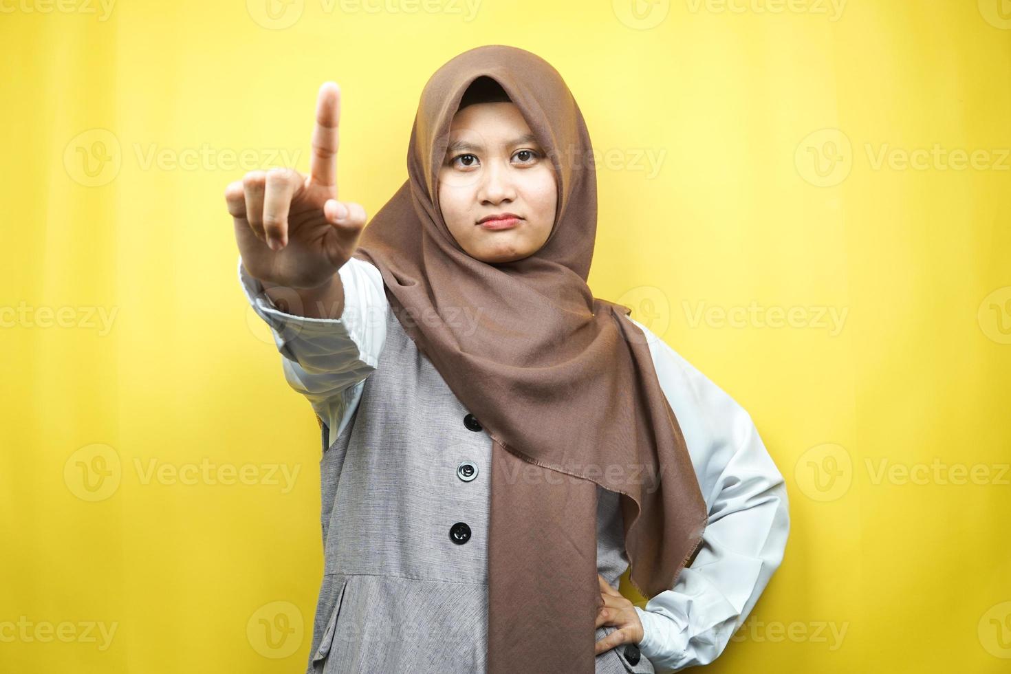 vacker självsäker asiatisk ung muslimsk kvinna, med nummer ett tecken hand, varningsskylt hand till kameran, isolerad på gul bakgrund foto