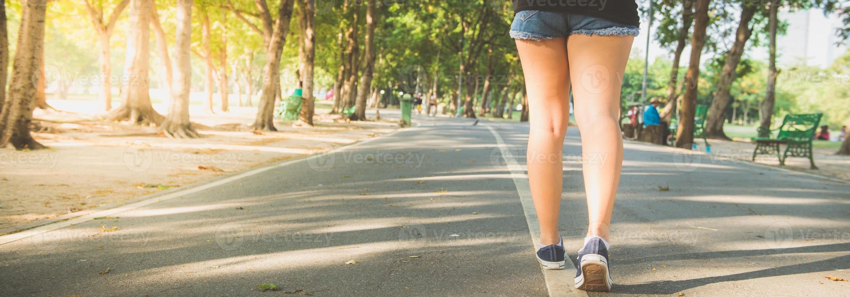 asiatisk kvinnas ben medan du joggar i parken täckt av massor av träd och varmt solljus. ung kvinna ben närbild när du springer i parken. utomhusaktivitet i parkkonceptet. panorama banner. foto