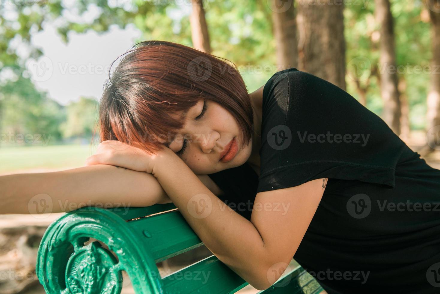 ung asiatisk kvinna sitter utomhus på den offentliga bänken och ligger längs bänken i parken i varmt solljus dag. ung kvinna koppla av hennes sinne och kropp i parken. utomhusaktivitet i parkkonceptet. foto