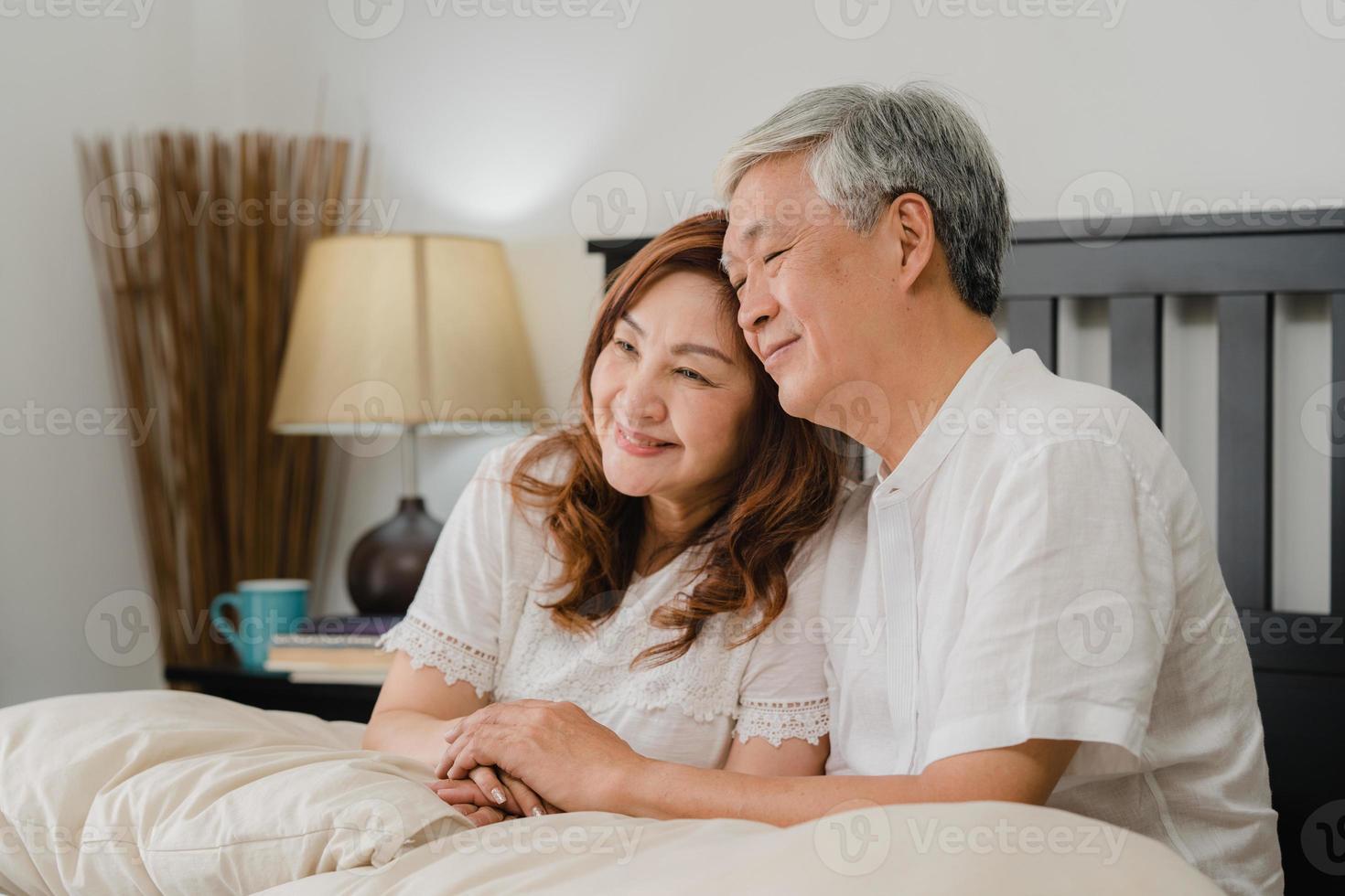 asiatiska senior par pratar på sängen hemma. asiatiska senior kinesiska farföräldrar, man och hustru kopplar gärna av tillsammans efter att ha vaknat medan de ligger på sängen i sovrummet hemma på morgonkonceptet. foto
