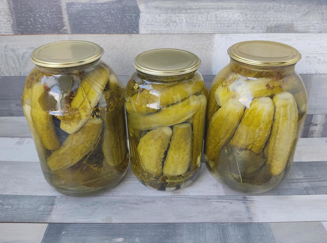 inlagda gurkor i en glasburk. tre stora burkar med pickles på bordet. förbereda mat och snacks för vintern. foto