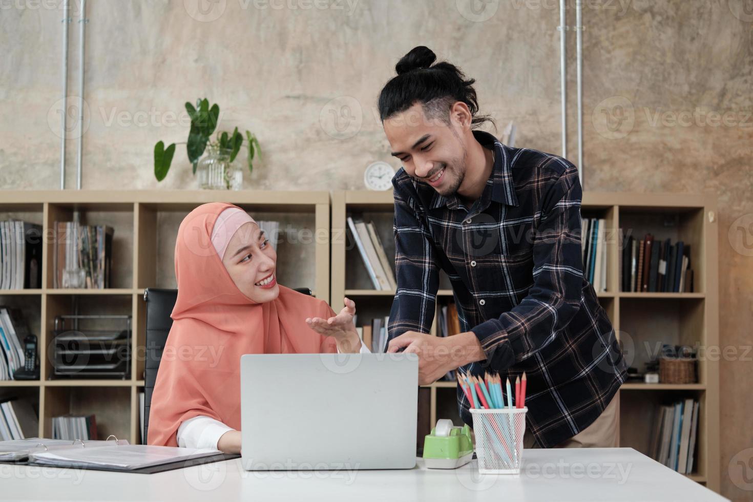 två unga startkollegor som är islamiska människor pratar om framgång med att arbeta i en e-handelsverksamhet med ett leende. använda bärbar dator till online -kommunikation via internet på ett litet kontor. foto