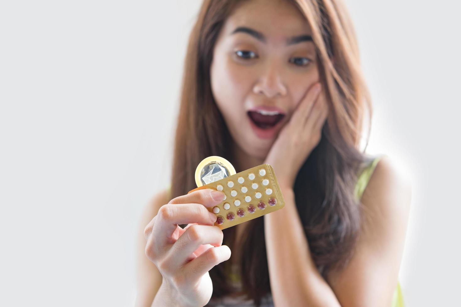 ung kvinna som håller kondom och p-piller förhindrar graviditet foto