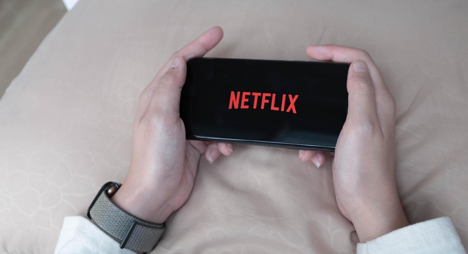 kvinna hand som håller smart telefon med Netflix logotyp på apple iphone xs. netflix är en global leverantör av strömmande filmer och tv-serier. foto