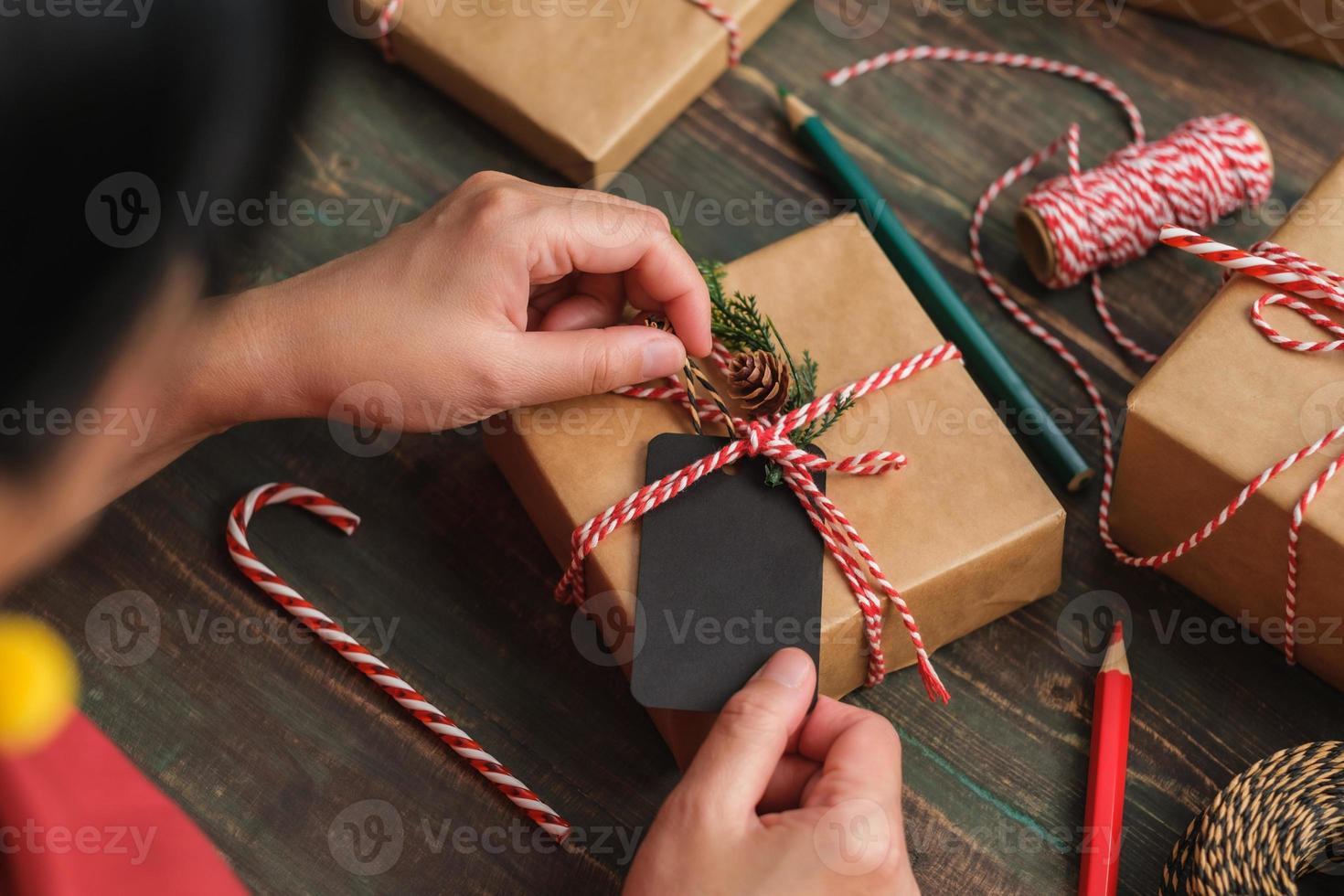 kvinna skriver presentetikett och fäst till julklapp på träbord foto