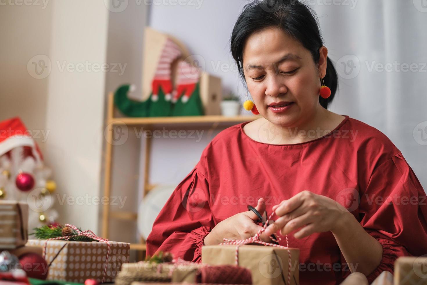 kvinna gör jul handgjorda presentförpackning med brunt papper skevning med xmas dekor på träbord foto