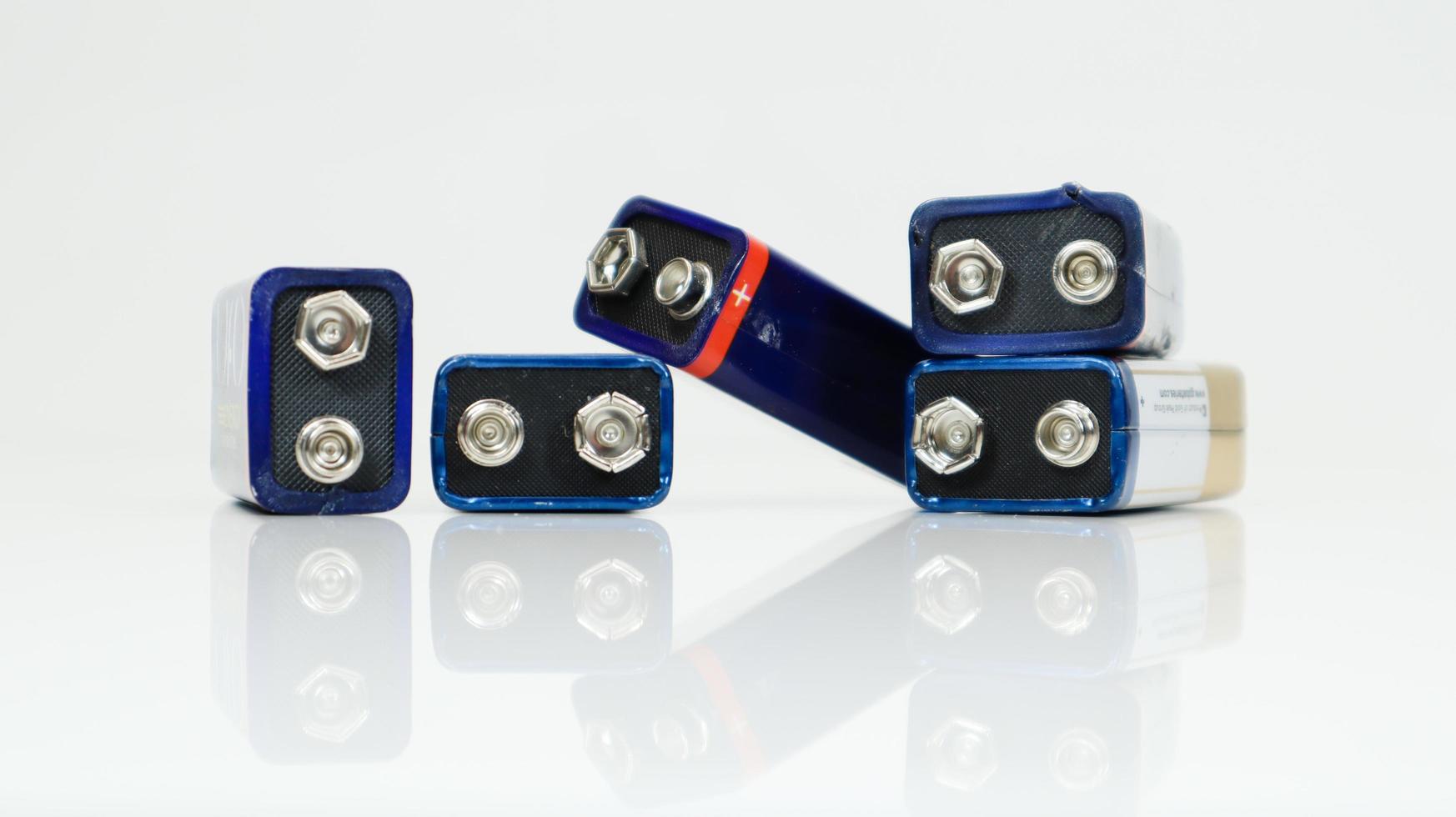 fem blå använda, kaotiskt upplagda och utspridda pp3-batterier på vit bakgrund med reflektion. huvudbatteri för personlig strömförsörjning. närbild av en repad och använd batterikontakt. foto