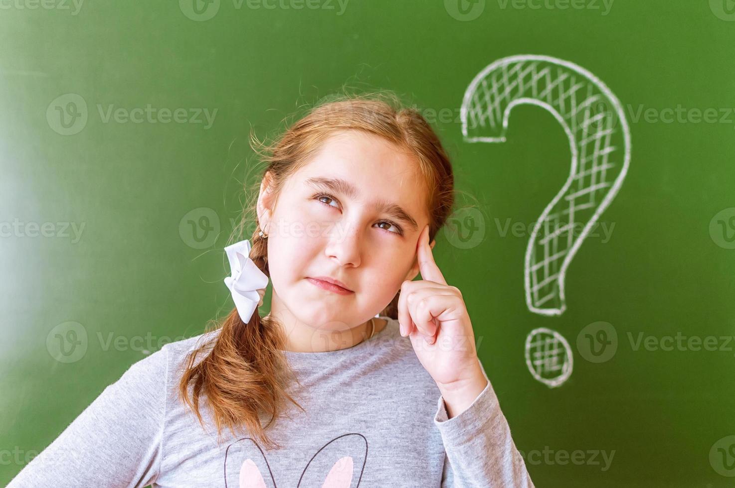 porträtt av en skolflicka som funderar på att lösa ett problem på tavlan under lektionen. foto