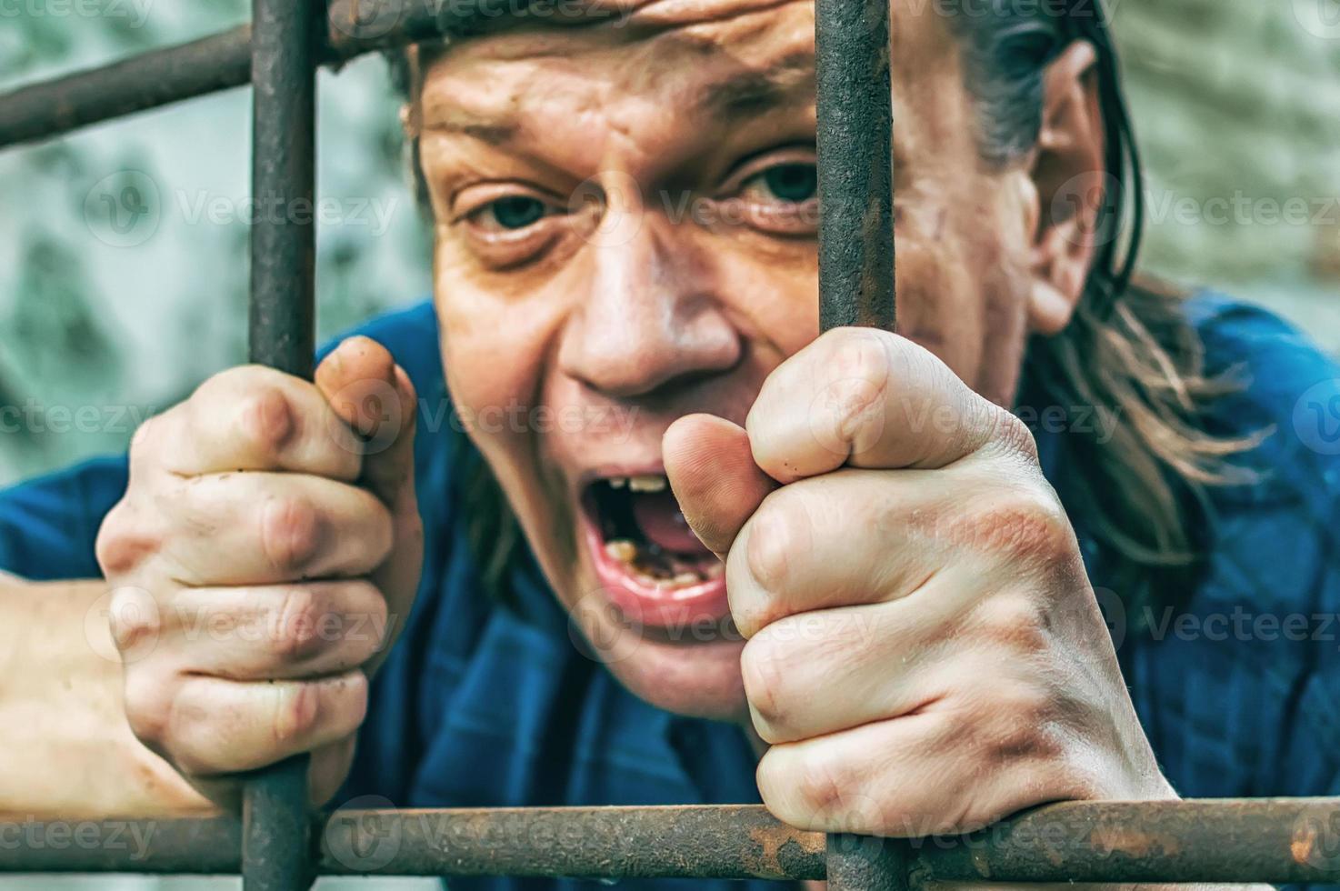 en deprimerad man i handbojor bakom galler. en deprimerad gripen manlig gärningsman sitter fängslad. skriker, rasar, gråter. foto