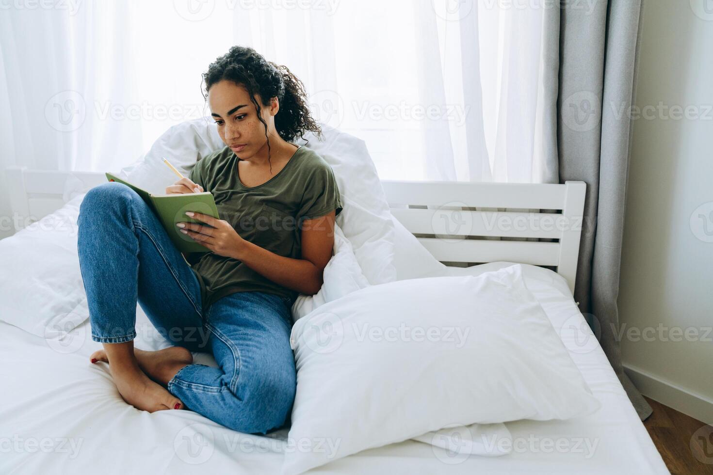 eftertänksam afrikansk kvinna skriver något i anteckningsblock på sängen foto