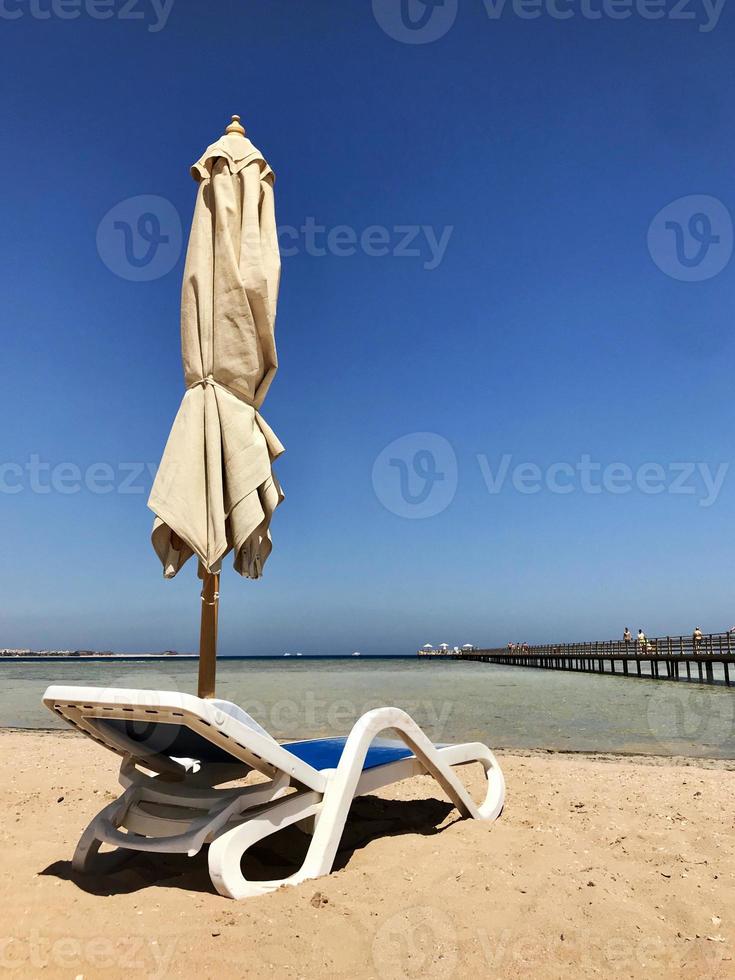 snygg solstol i gul sand till solstol på stranden på sommaren under öppen himmel foto