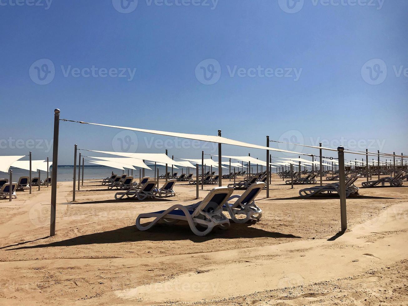 snygg solstol i gul sand till solstol på stranden på sommaren under öppen himmel foto