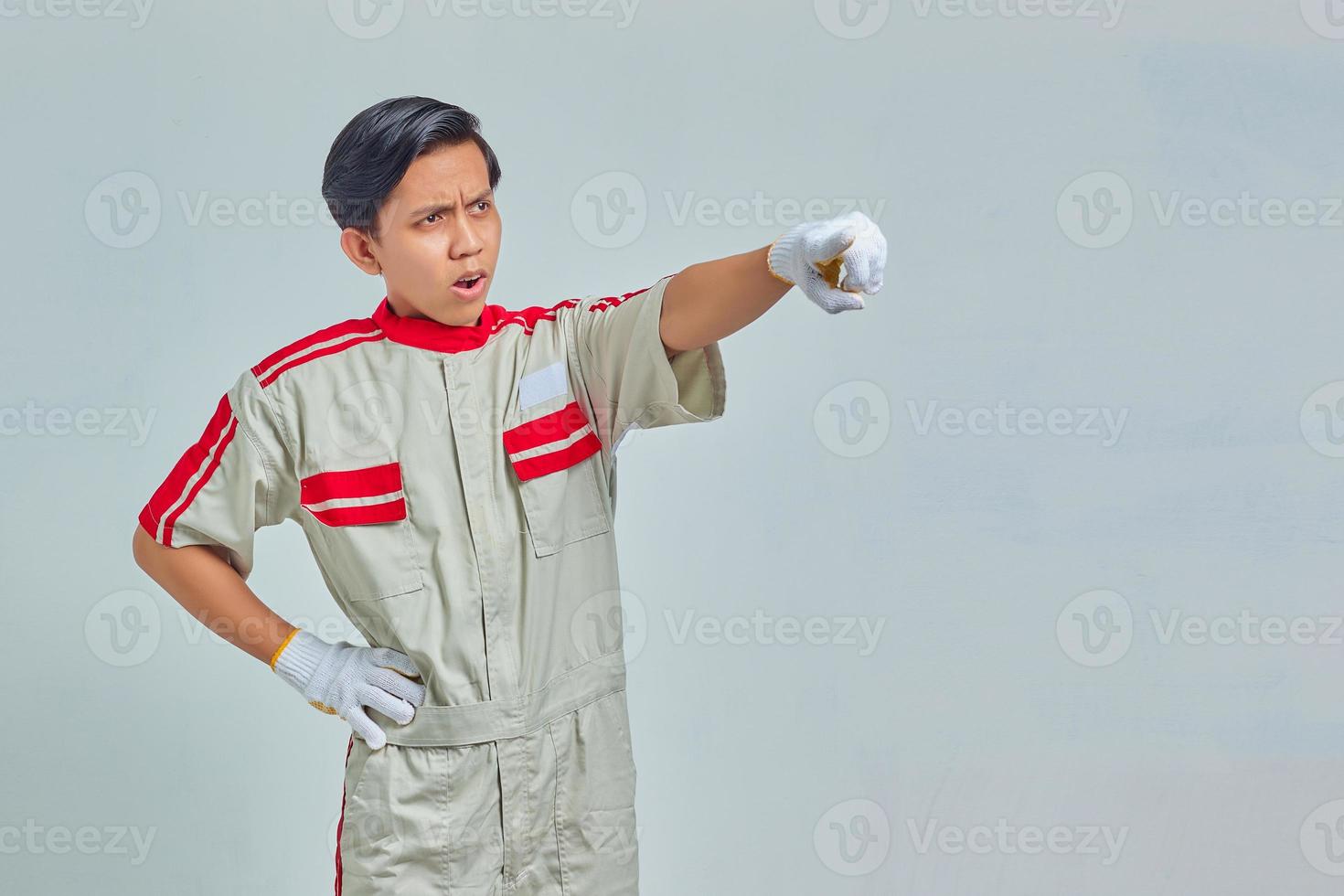 porträtt av förvånad stilig man som bär mekanisk uniform pekar med öppet finger och mun på grå bakgrund foto