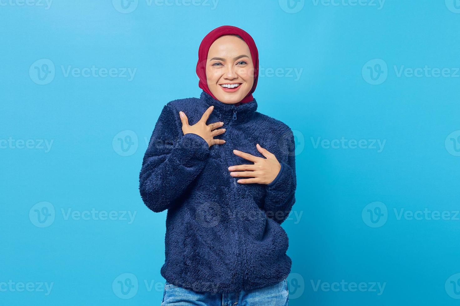 glad ung asiatisk kvinna lägger en hand på en kista och tittar på kameran på blå bakgrund foto