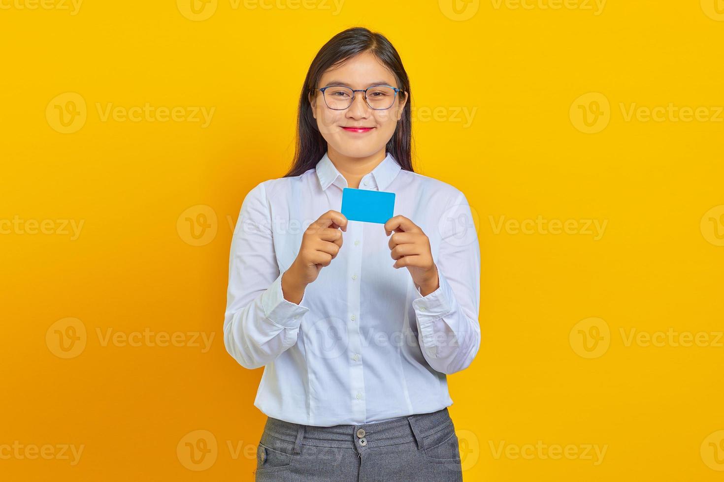porträtt av leende ung asiatisk kvinna som visar kreditkort på gul bakgrund foto
