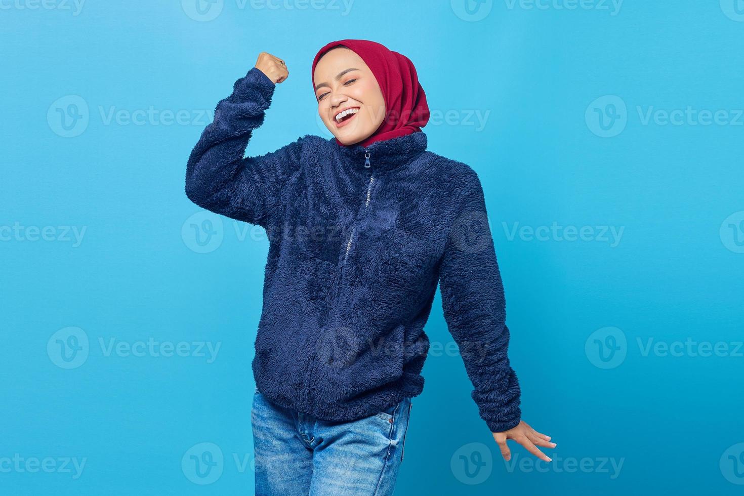 porträtt av upphetsad ung asiatisk kvinna som firar framgång på blå bakgrund foto