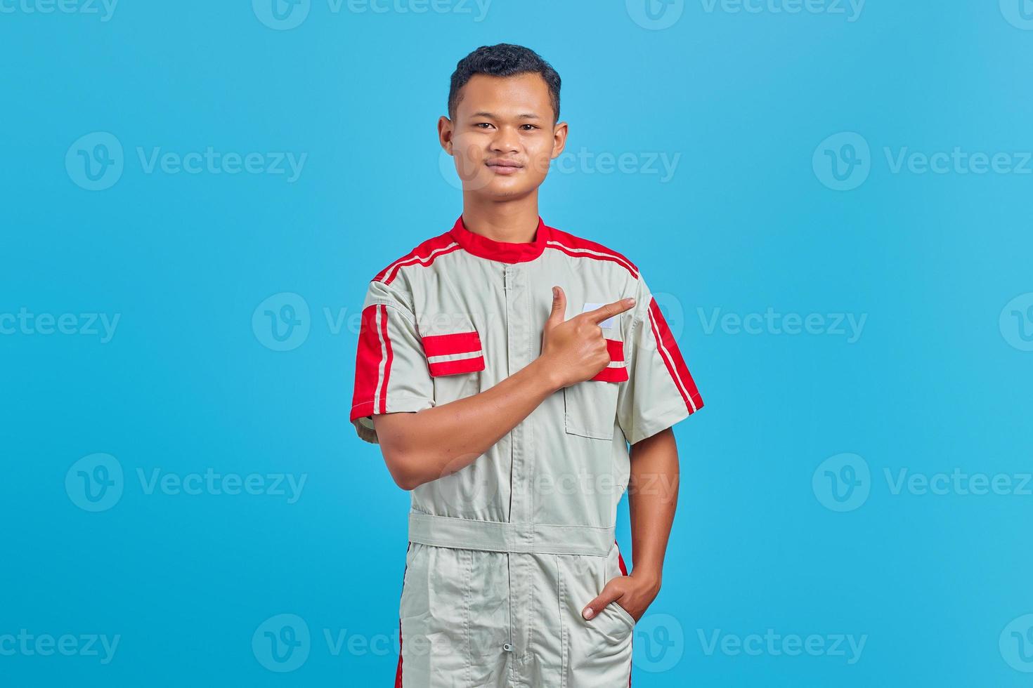 porträtt av leende ung mekaniker pekar finger på kopia utrymme på blå bakgrund foto