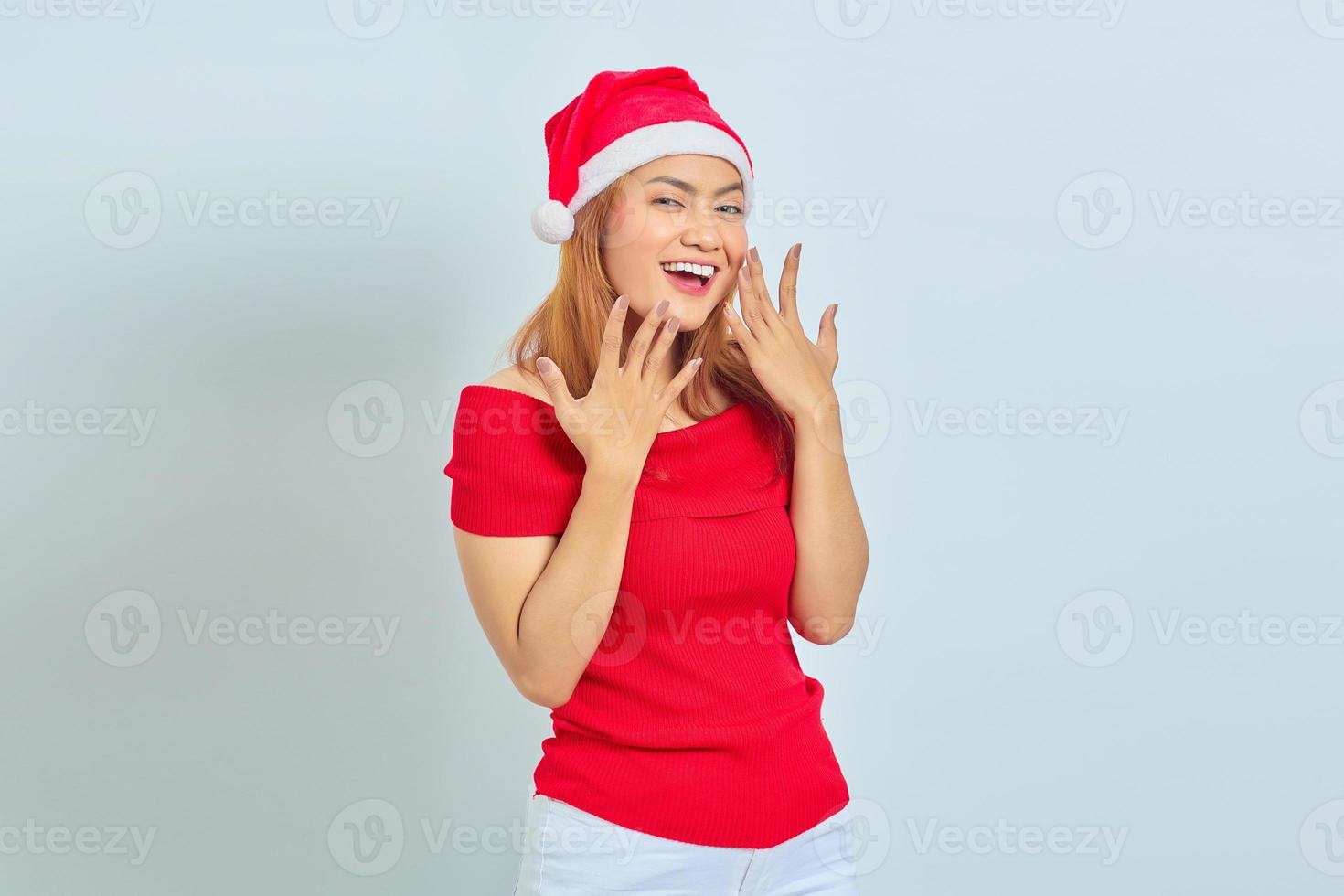 porträtt av glad ung asiatisk kvinna i julhatt höja händerna över vit bakgrund foto
