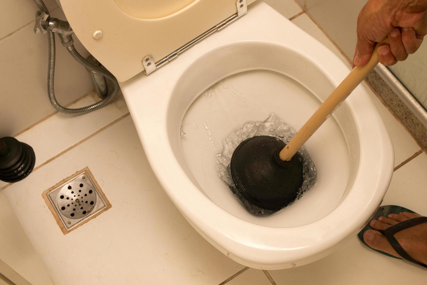 man som använder en kolv för att stoppa sitt handfat i badrummet foto