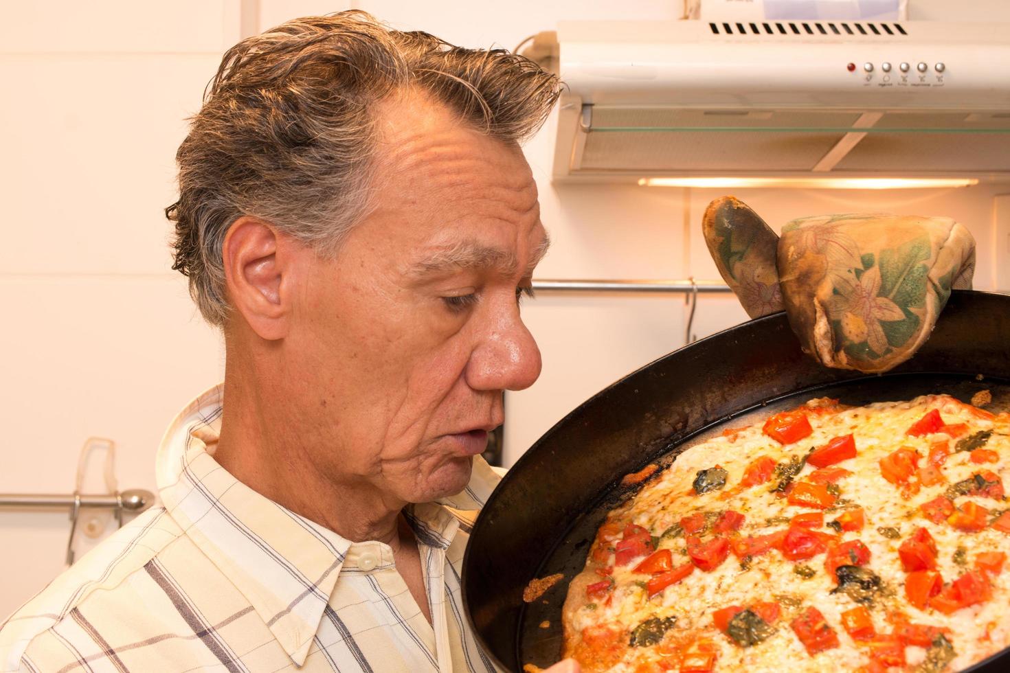 mogen man i sitt kök som beundrar sin hemmagjorda pizza margherita foto