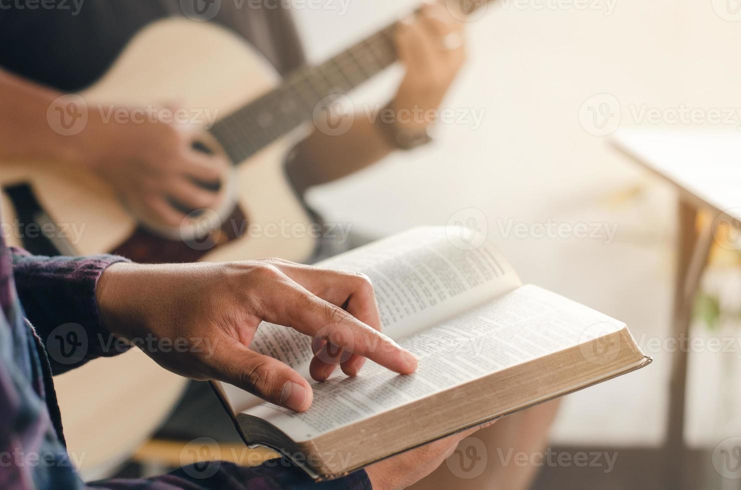 en ung pojke satt och läste i Bibeln medan hans vän spelade gitarr i kyrkan när han tillbad gud. en liten grupp kristna eller ett koncept i en kyrka vid en kyrka foto