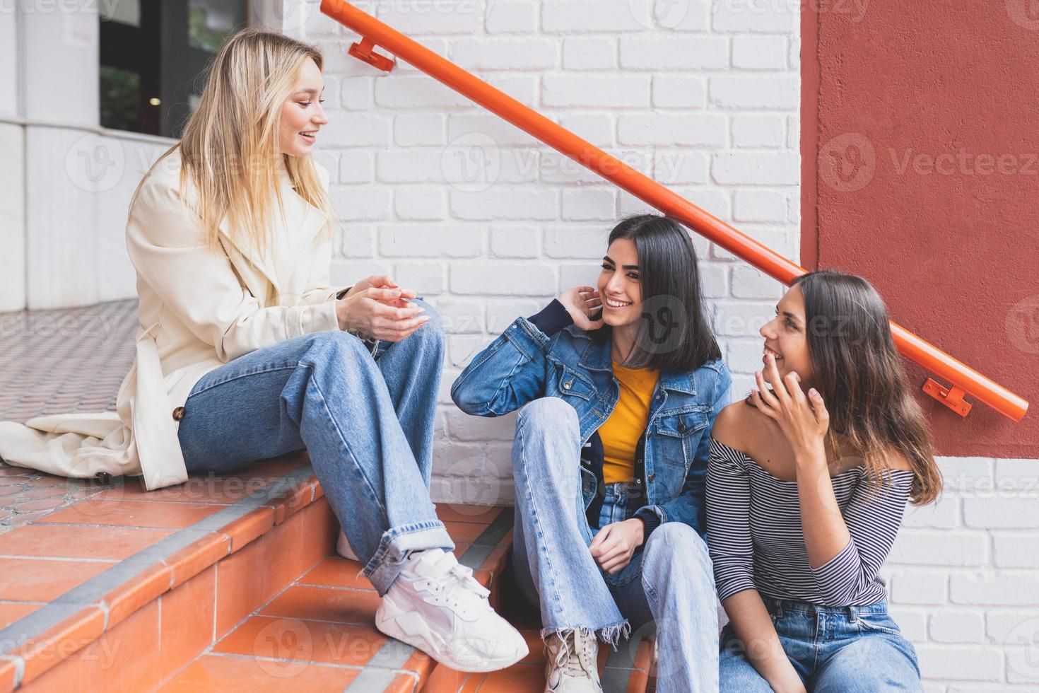 multietnisk grupp av tre vänner som sitter på gatutrappan och pratar. foto