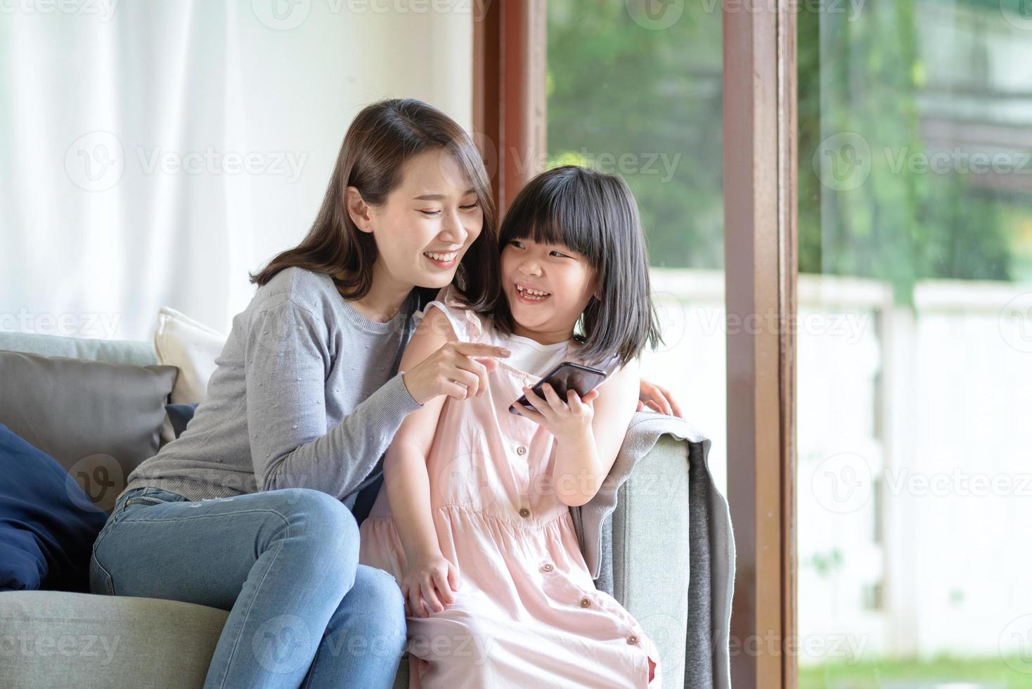 asiatisk mamma och hennes dotter tycker om att använda internet via smart telefon hemma foto