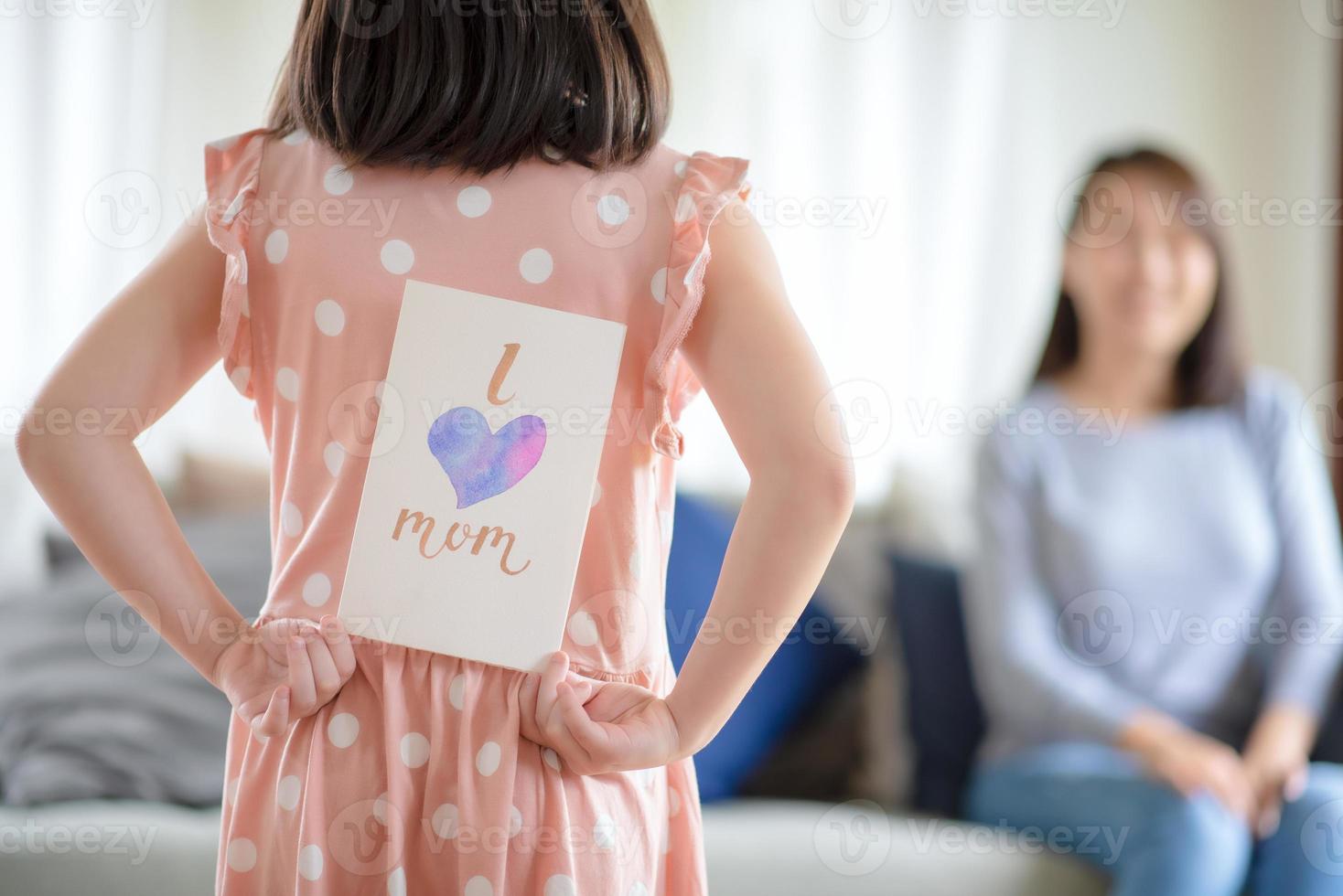 asiatisk söt tjej gömmer handgjort gratulationskort med jag älskar mamma ord att ge överraska sin mamma hemma foto