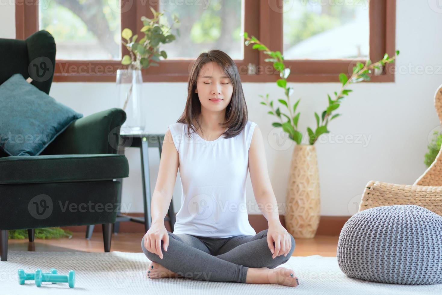 vacker asiatisk kvinna behåll lugnet och mediterar medan du övar yoga hemma för en hälsosam trendlivsstil foto