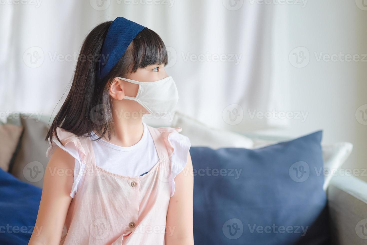 asiatisk liten söt tjej som bär en hygienisk ansiktsmask för att förhindra coronavirus eller covid-19-utbrott, håll social distans och stanna hemma. foto