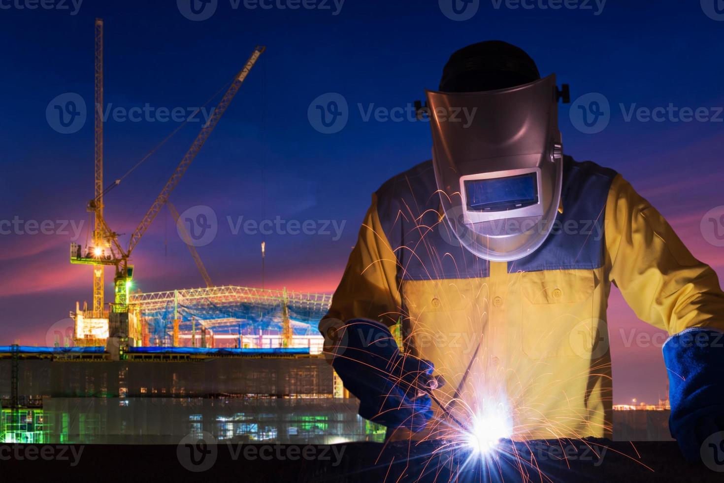 industriarbetare som svetsar stålkonstruktion för infrastrukturbyggnadsprojekt med byggarbetsplats i bakgrunden. foto