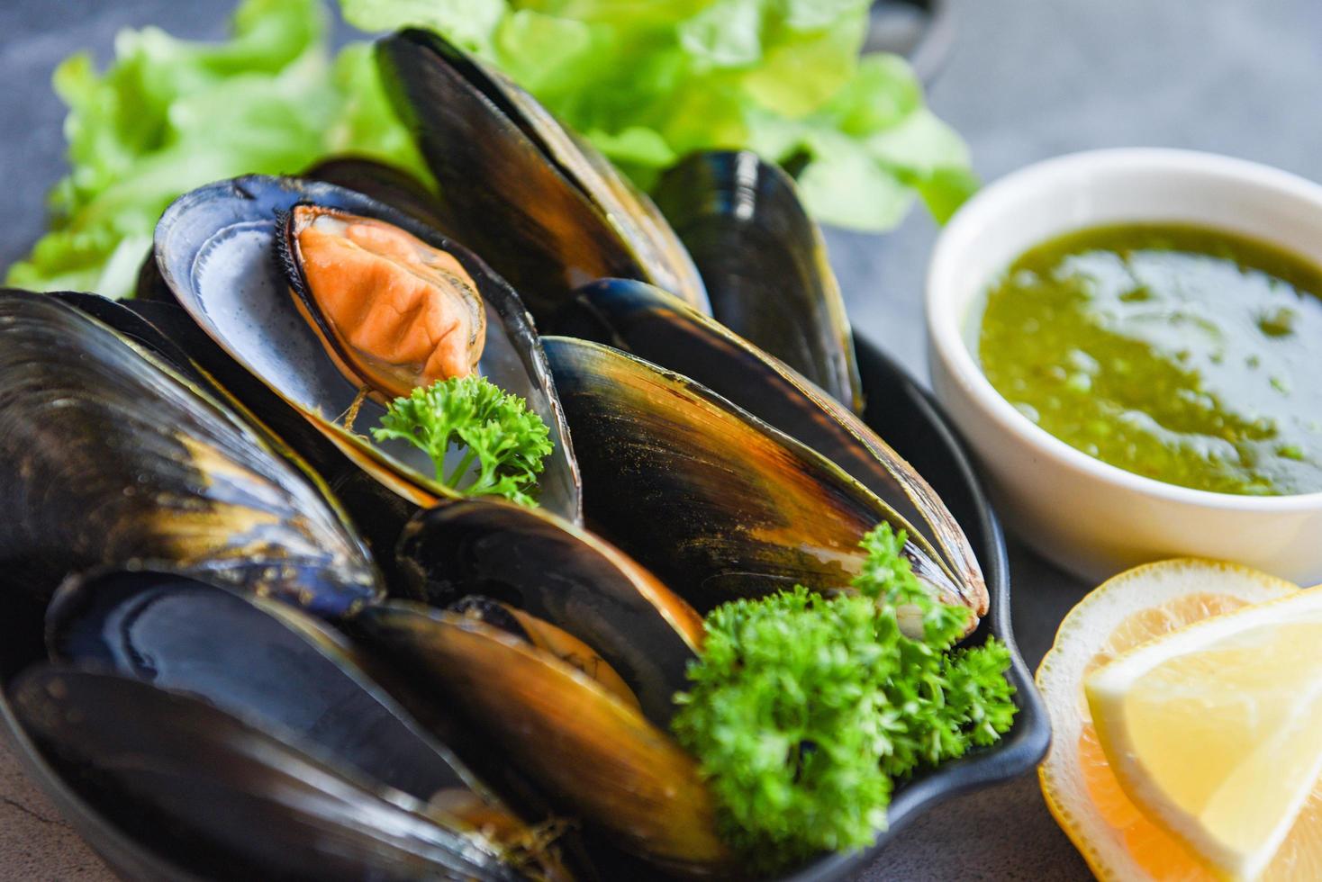 kokta musslor med örter citron och mörk tallrikbakgrund - färska skaldjursskaldjur på skål och kryddig sås i restaurangen musselmat foto