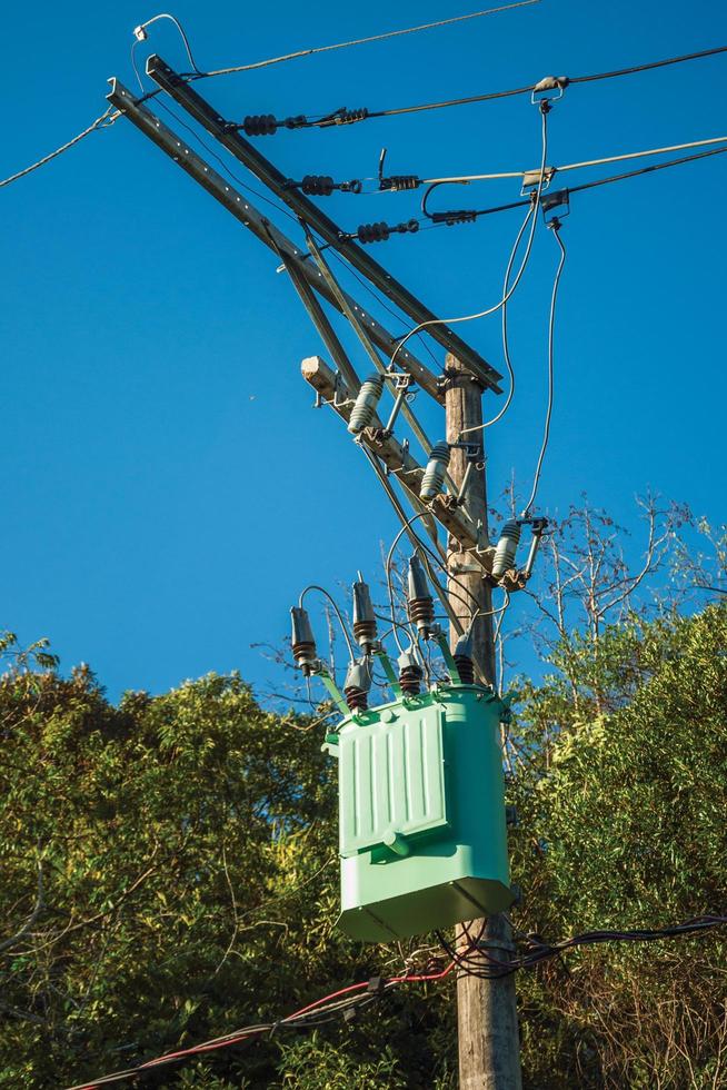 detalj av högspänningskraftstolpetransformator med elektriska ledningar framför träd nära gramado. en söt europeisk influerad stad i södra Brasilien mycket eftertraktad av turister. foto