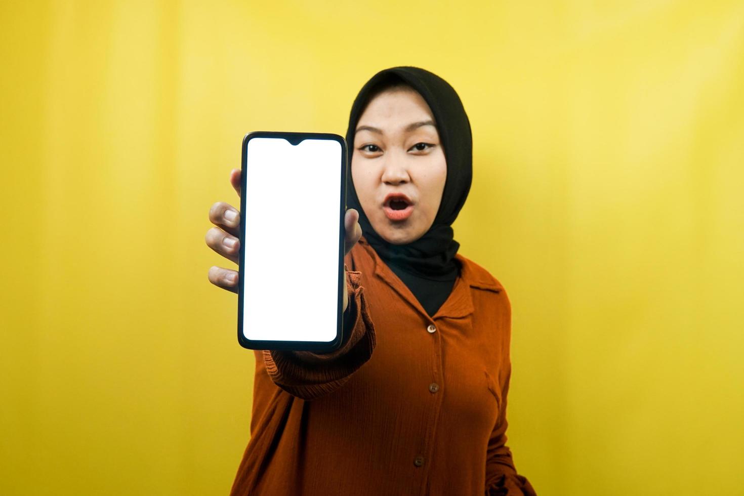 vacker ung asiatisk muslimsk kvinna chockad, förvånad, wow-uttryck, handhållen smartphone med vit eller tom skärm, marknadsför app, marknadsför produkt, presenterar något, isolerad foto