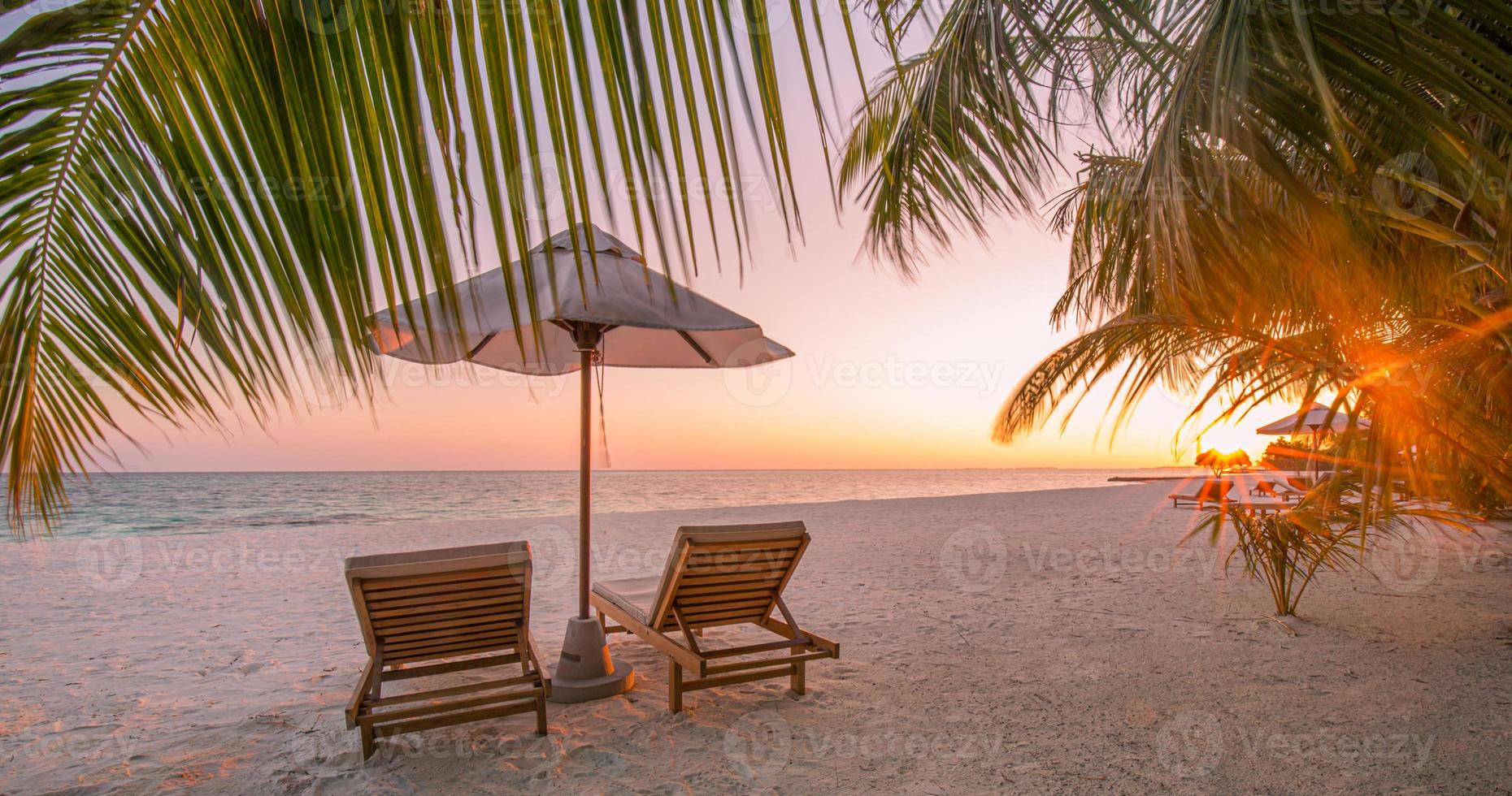 vackert tropiskt solnedgångslandskap, två solstolar, solstolar, paraply under palmen. vit sand, havsutsikt med horisont, färgglad skymningshimmel, lugn och avkoppling. inspirerande strandhotell foto