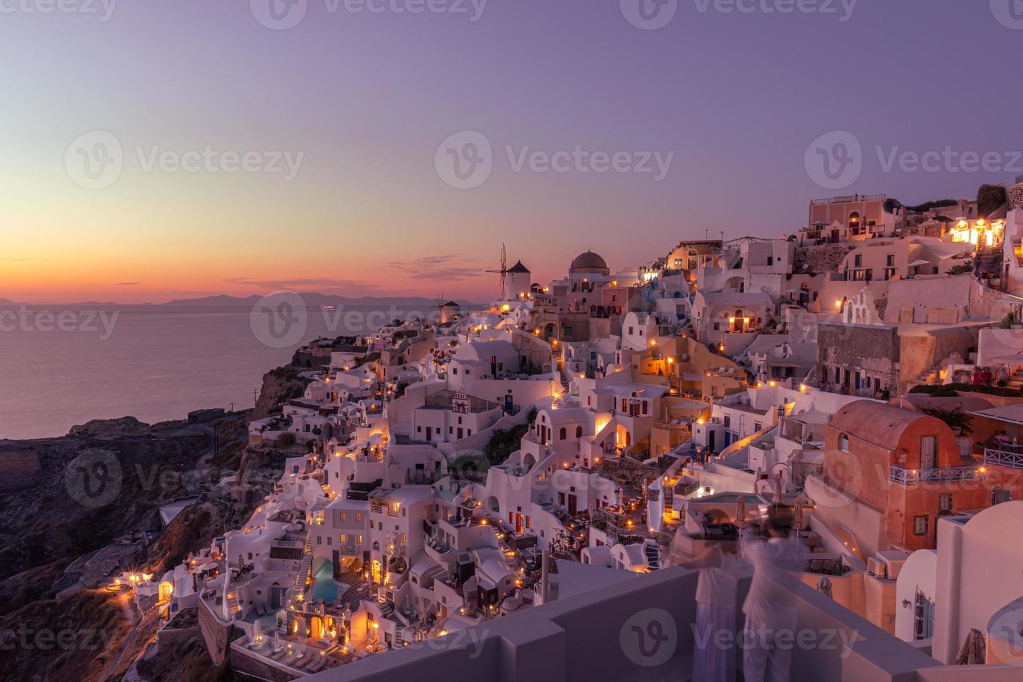 solnedgång på ön santorini grekland, vacker vitkalkade by oia med kyrka och väderkvarn under solnedgången, gator i oia santorini under sommarsemester på den grekiska ön foto